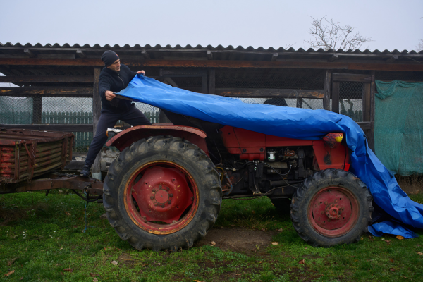 320GSM extra heavy-duty waterproof PE tarp being used by farmer to cover tractor – durable UV-stabilised tarpaulin Australia